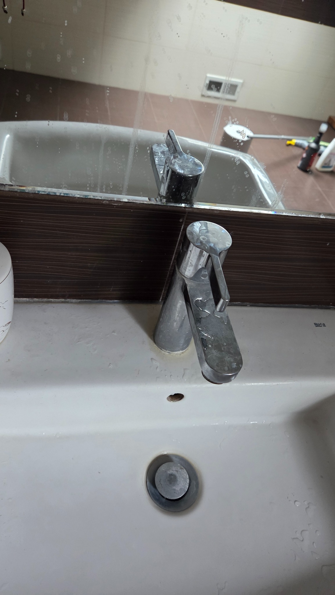 Zlew z brudną baterią i lustrem z zaciekami. Widoczne ślady po czyszczeniu. Potrzeba dokładnego umycia i usunięcia osadów.