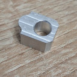 JDATech - Szlifowany, aluminiowy element z otworem, leżący na drewnianej powierzchni, z widocznymi śladami obróbki.