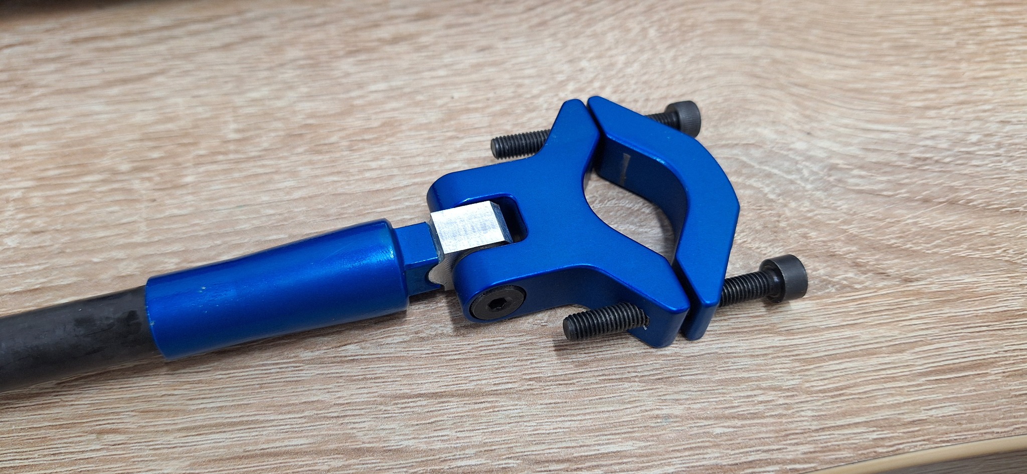 Niebieski, anodowany zacisk mocujący z czarnymi śrubami na drewnianym tle, element konstrukcyjny z aluminium.