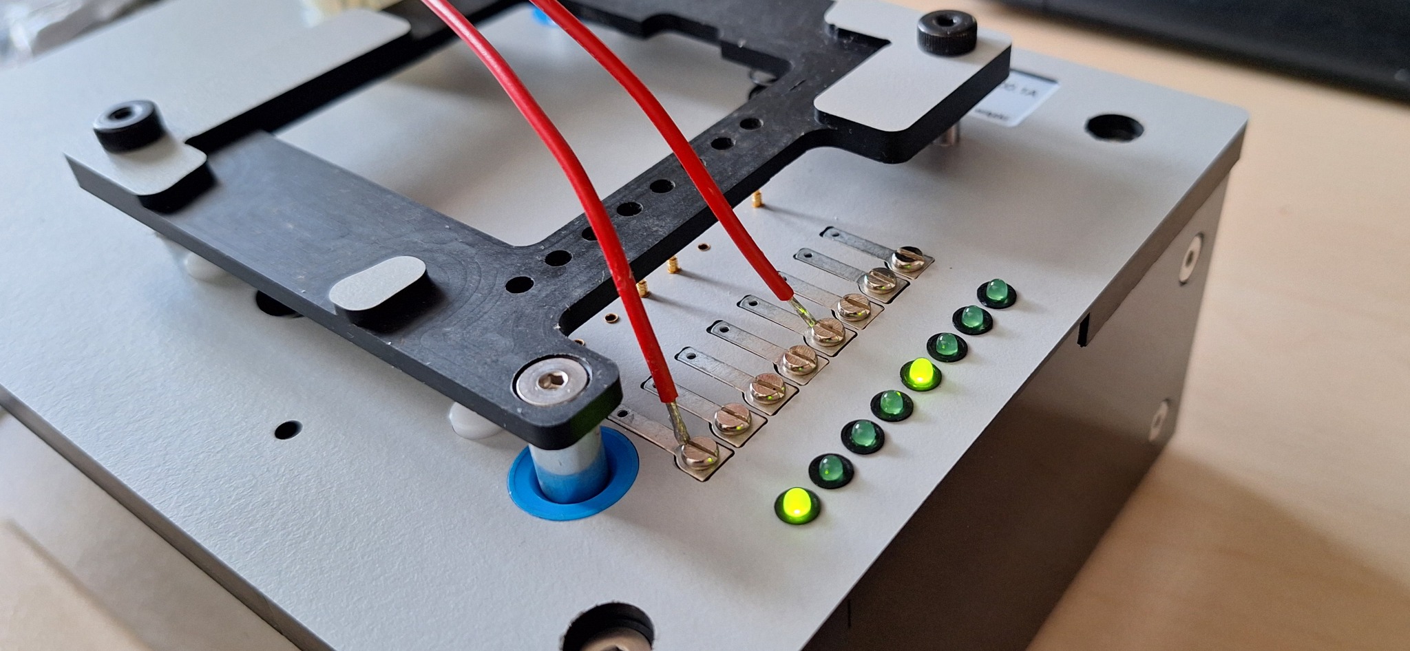 Detale złącza testowego CNC z podłączonymi czerwonymi przewodami i świecącymi diodami LED, widoczne śruby mocujące.