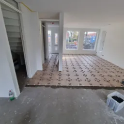 Układanie brązowych płytek podłogowych z użyciem krzyżyków dystansowych w przestronnym, jasnym pomieszczeniu w trakcie prac wykończeniowych.