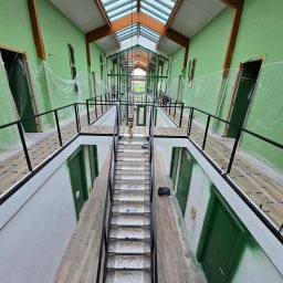 KONKRET Zbigniew Stańczak - Wnętrze budynku w trakcie prac wykończeniowych: świeżo pomalowane na zielono ściany, drewniana konstrukcja dachu z przeszkleniami, schody z zabezpieczeniami na stopniach, podłoga wyłożona panelami,...