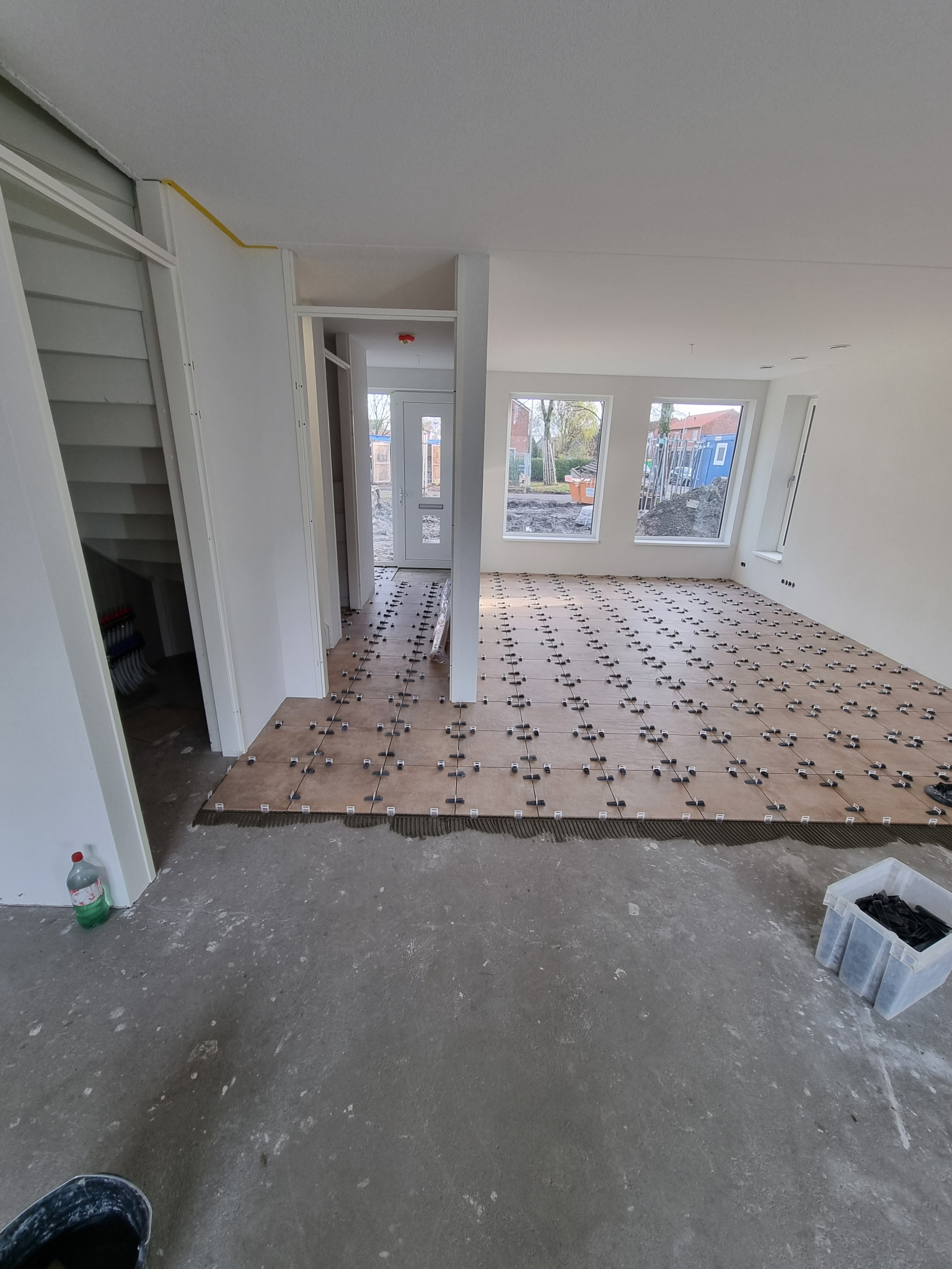 Układanie brązowych płytek podłogowych z użyciem krzyżyków dystansowych w przestronnym, jasnym pomieszczeniu w trakcie prac wykończeniowych.