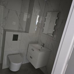 REMONTY PK TOMASZEWSCY SPÓŁKA Z OGRANICZONĄ ODPOWIEDZIALNOŚCIĄ - Nowoczesna łazienka z marmurowymi płytkami, wiszącą toaletą i białą szafką umywalkową. Minimalistyczny design, szara podłoga i lustro z oświetleniem.