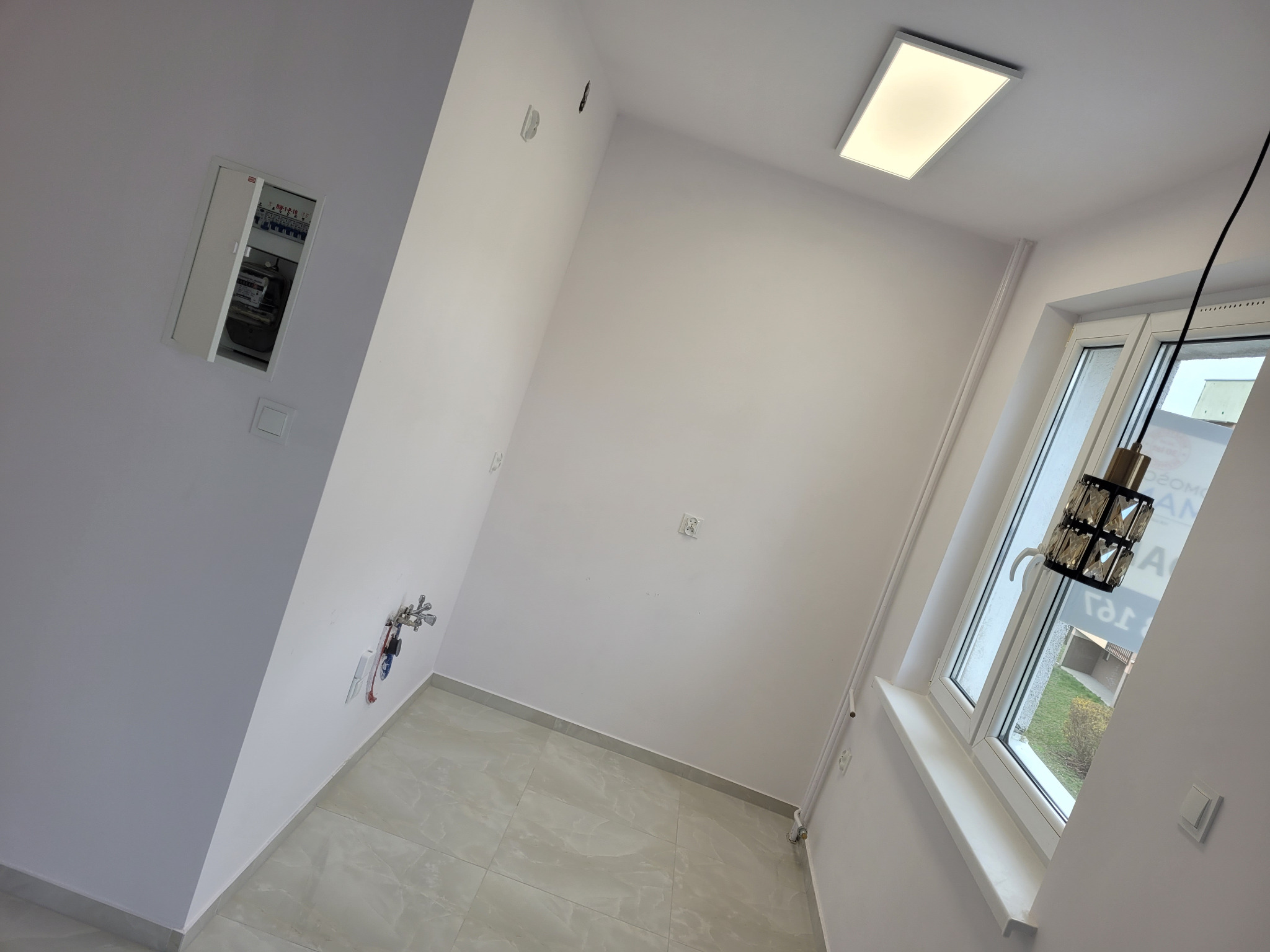 Wykończona łazienka w Złotowie: białe ściany, szara podłoga z płytek, okno z widokiem na zieleń i nowoczesna lampa wisząca. Widoczna instalacja wodna i elektryczna.