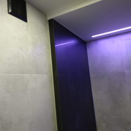 JARDAR SPÓŁKA Z OGRANICZONĄ ODPOWIEDZIALNOŚCIĄ - Nowoczesna łazienka z ciemną ścianą akcentującą, oświetleniem LED i szarą płytką imitującą beton, widoczny fragment wentylacji.