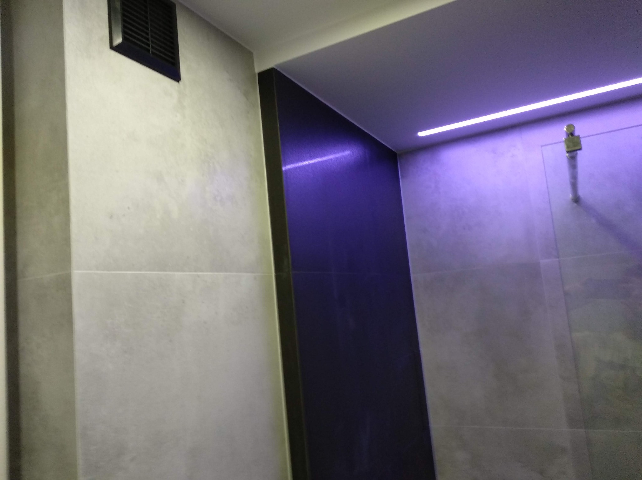 Nowoczesna łazienka z ciemną ścianą akcentującą, oświetleniem LED i szarą płytką imitującą beton, widoczny fragment wentylacji.