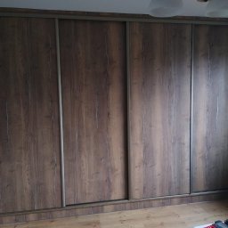 DrewnaMoc - Duża szafa wnękowa z przesuwnymi drzwiami o wzorze ciemnego drewna i srebrnych prowadnicach, widoczna na tle parkietu.