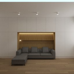 DrewnaMoc - Minimalistyczny salon: zabudowa meblowa z wnęką oświetloną ciepłym światłem, w której umieszczono szarą sofę z szezlongiem, drewniana podłoga.