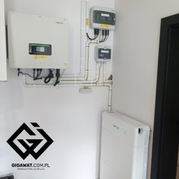 GE GIGAWAT SPÓŁKA Z OGRANICZONĄ ODPOWIEDZIALNOŚCIĄ - Zainstalowany falownik hybrydowy Sofar oraz magazyn energii Sofar BTS 10kWh z modułem zasilania rezerwowego, widoczne białe rury instalacyjne i skrzynki elektryczne na białej ścianie w pomieszczeniu.