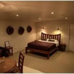 Rustykalna sypialnia z drewnianym łóżkiem i lampą w stylu vintage. Na ścianie dekoracje z wikliny. Ciepłe oświetlenie tworzy przytulny klimat.