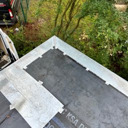 DACHY, TARASY, BALKONY, PIOTR BURLITA - Widok z góry na fragment dachu z nową, czarną membraną hydroizolacyjną KSA DUO, obróbki blacharskie z jasnego metalu i częściowo zamontowaną blachą trapezową, w tle zieleń drzew i samochód firmy...