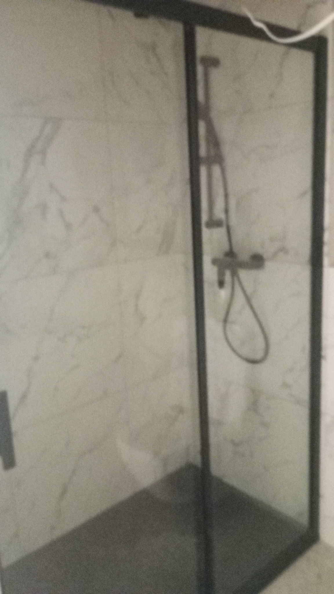 Kabina prysznicowa z czarną ramą i marmurowymi płytkami w tle, widok z boku.