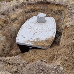 Mini Kop Eryk Kujawa - Montaż szamba betonowego w wykopie, widoczne ślady pracy koparki, w tle pole i drzewa.