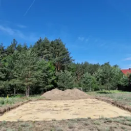 Przygotowany, wyrównany teren pod budowę z wykopanymi obrysami fundamentów i usypaną pryzmą ziemi w tle, widok w słoneczny dzień.