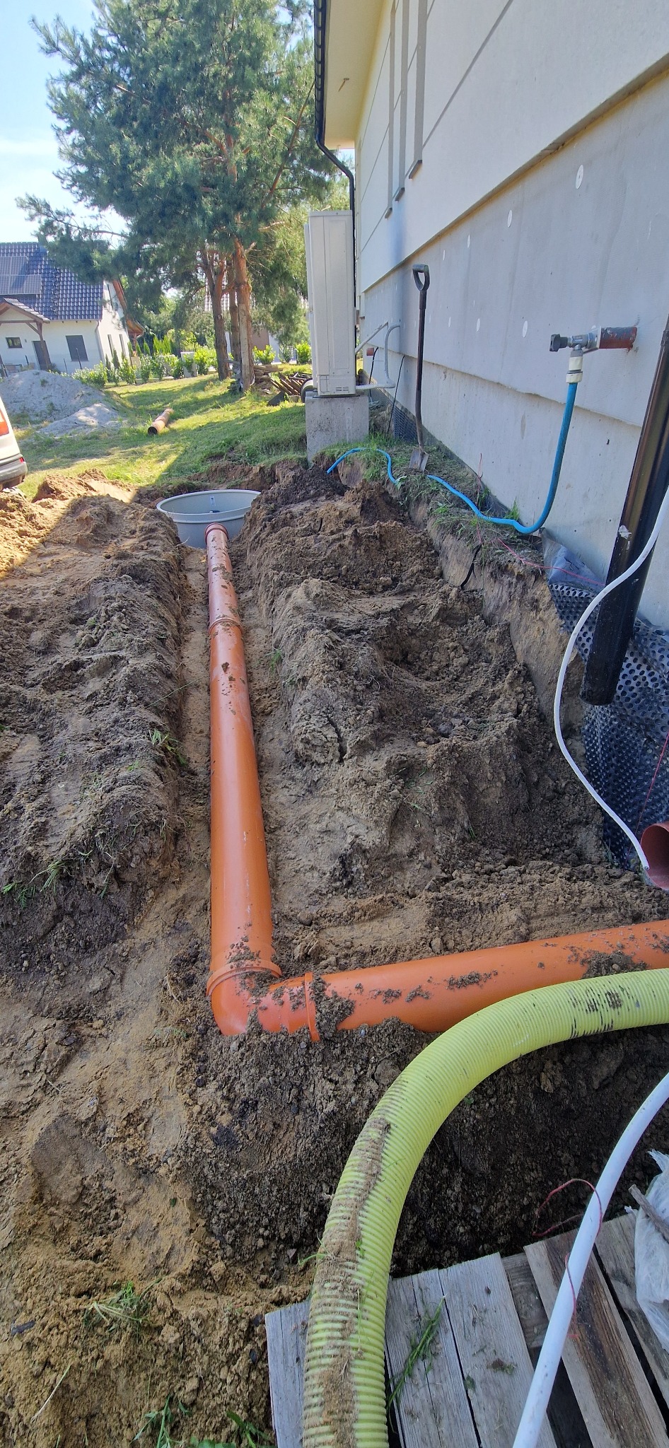 Wykop w ziemi z ułożonymi rurami kanalizacyjnymi z tworzywa sztucznego, studzienka rewizyjna, widoczne elementy instalacji przy budynku.