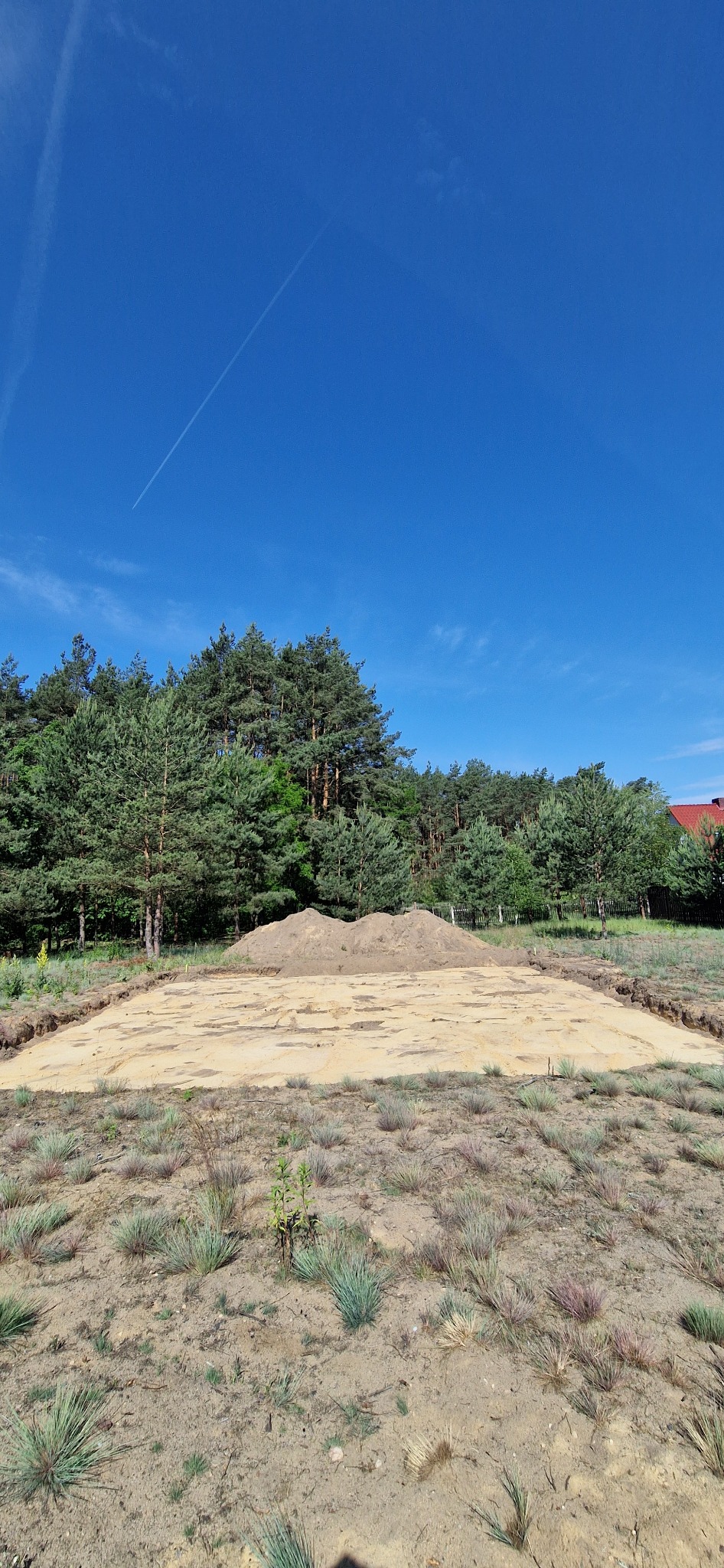 Przygotowany, wyrównany teren pod budowę z wykopanymi obrysami fundamentów i usypaną pryzmą ziemi w tle, widok w słoneczny dzień.