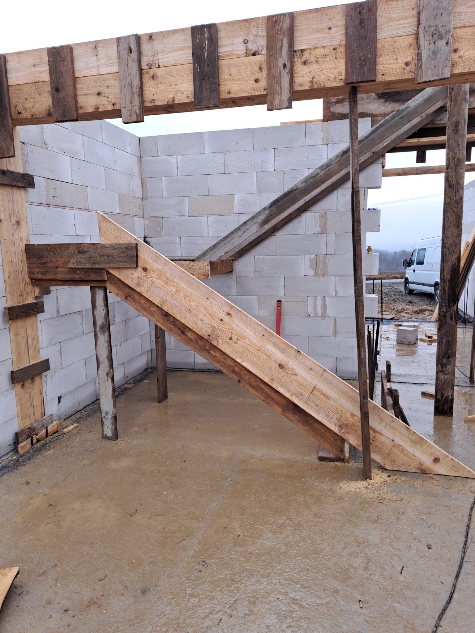 Wznoszenie ścian z betonu komórkowego Ytong z widocznym szalunkiem i podporami drewnianymi, mokra posadzka i poziomica w tle.