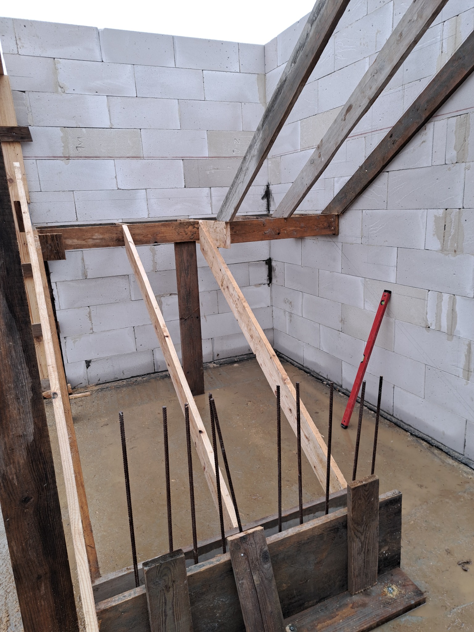 Wykop pod budynek z drewnianym szalunkiem, wystającymi prętami zbrojeniowymi i ścianami z białych bloczków, poziomica oparta o ścianę.