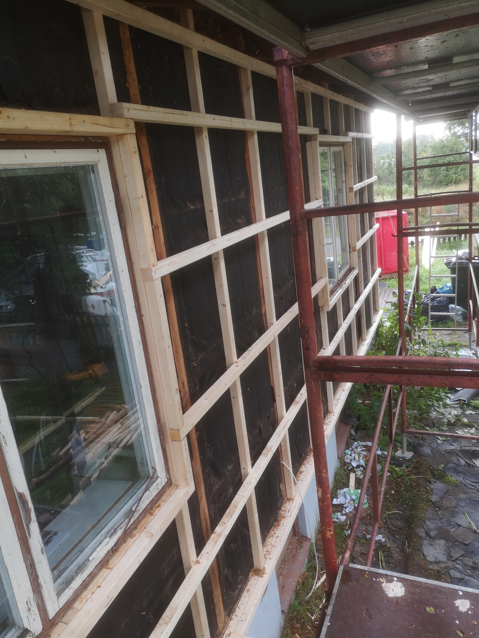 Drewniana konstrukcja szkieletowa na elewacji budynku z widocznym oknem i rusztowaniem; przygotowanie do ocieplenia.