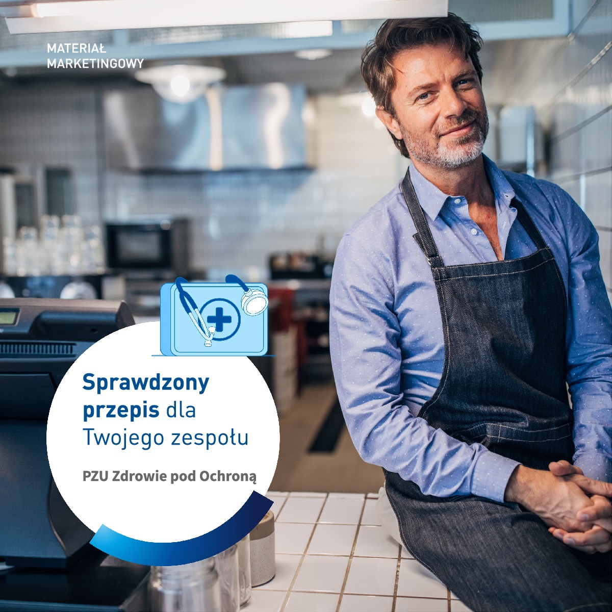 Uśmiechnięty mężczyzna w dżinsowym fartuchu siedzi na blacie w kuchni restauracyjnej, obok grafiki z napisem 'Sprawdzony przepis dla Twojego zespołu PZU Zdrowie pod Ochroną'.