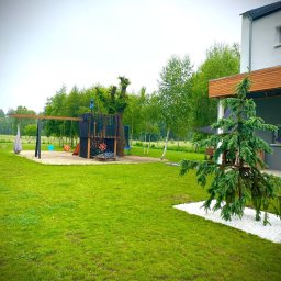 PKUBI-BAU Piotr Kubiciel - Rozległy, zielony trawnik w Ozimku z nowoczesnym placem zabaw w tle, obok domu z dekoracyjnym świerkiem na białym żwirze.
