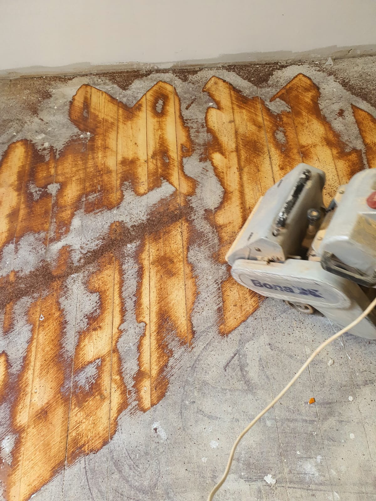 Szlifowanie drewnianej podłogi maszyną Bona, widoczne ślady po cyklinowaniu i pył drzewny na surowym parkiecie.