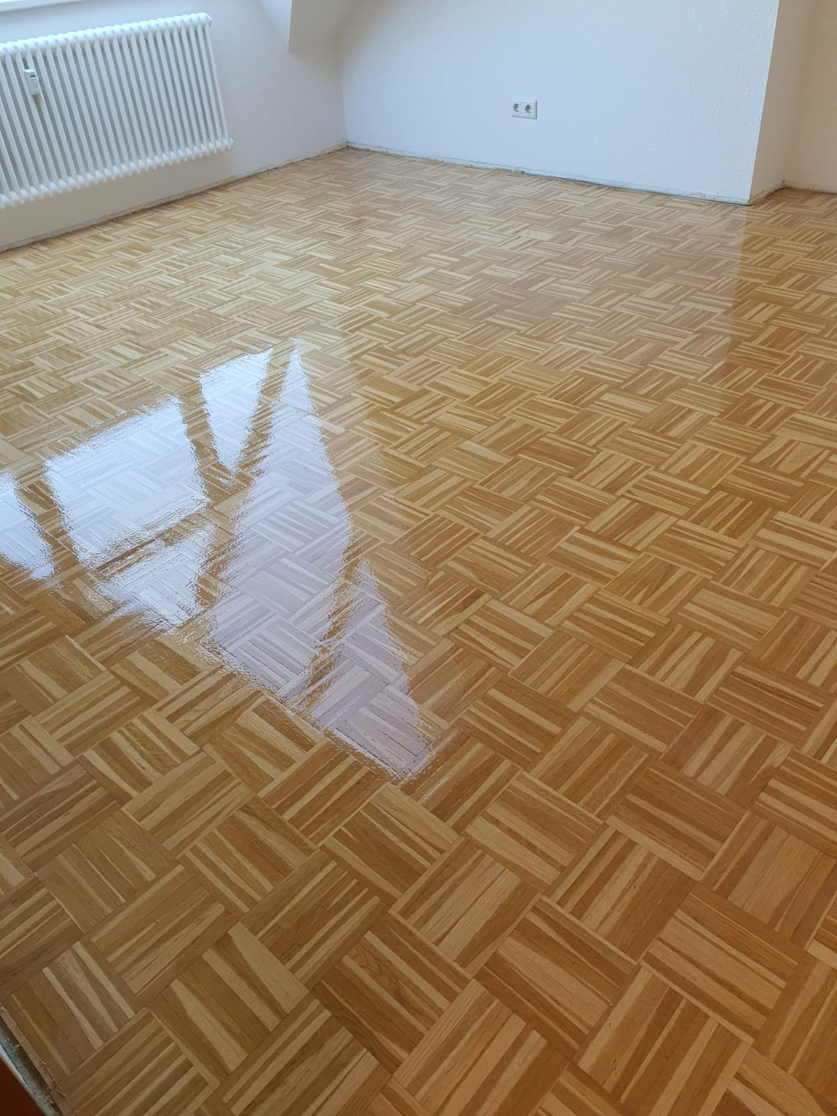 Wypolerowany parkiet w jodełkę, z widocznym odbiciem okna, po cyklinowaniu i lakierowaniu.