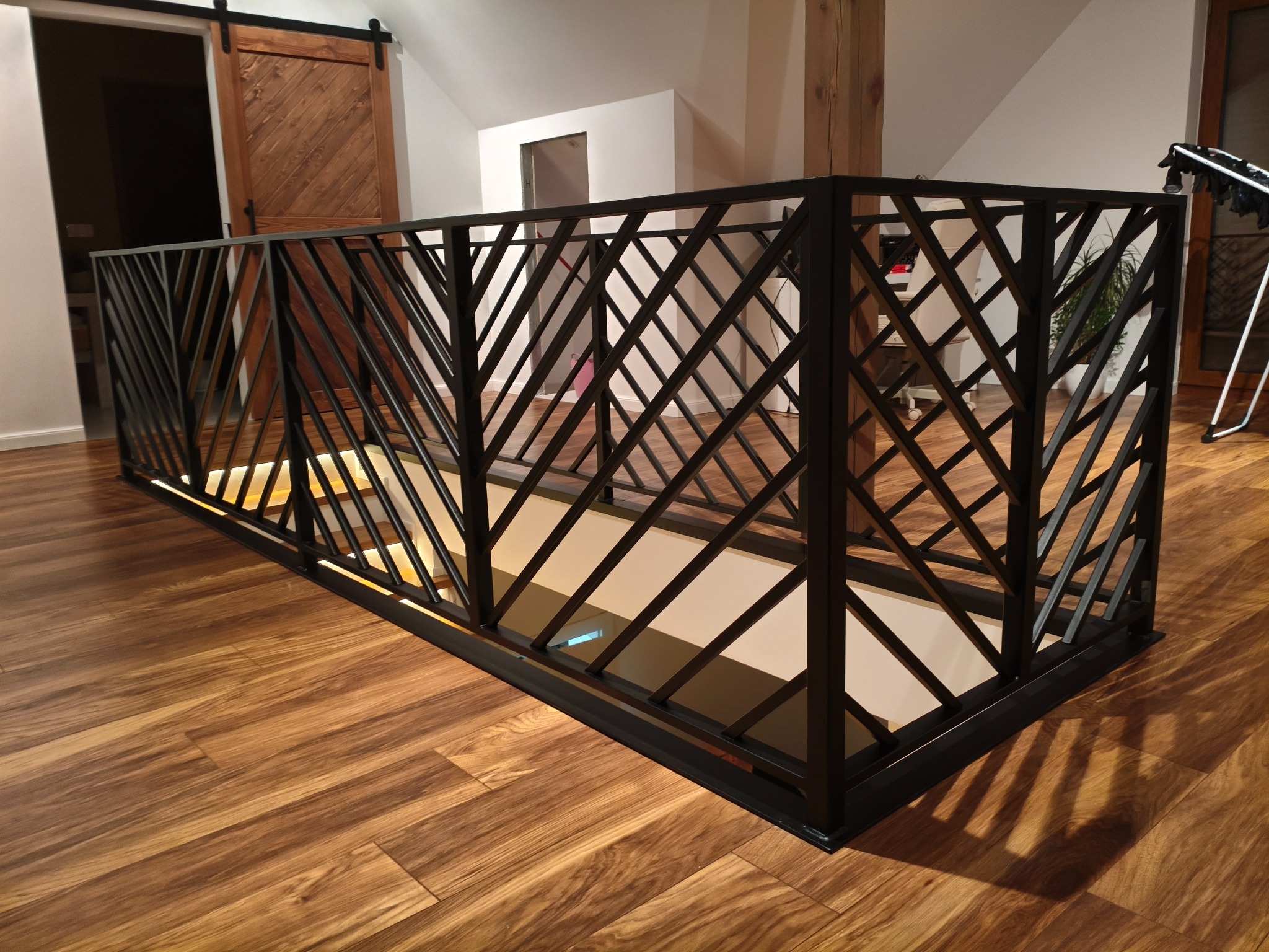 Nowoczesna balustrada metalowa w geometryczny wzór, zabezpieczająca schody wewnątrz domu. Realizacja z Osin, widok z góry na drewnianą podłogę.