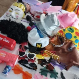 Akcesoria do przebrania na białym stole: maski, peruki, kapelusze, okulary w kształcie serc, korona, zabawkowy pistolet na bańki.