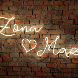 Hubert Ploch Media - Neonowy napis 'Żona Mąż' z sercem pośrodku, umieszczony na tle ściany z czerwonej cegły.