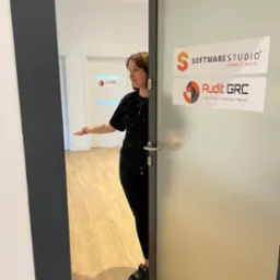 Pracownica biura rachunkowego Audit GRC zaprasza do środka, widoczne logo firmy na szklanych drzwiach wejściowych.