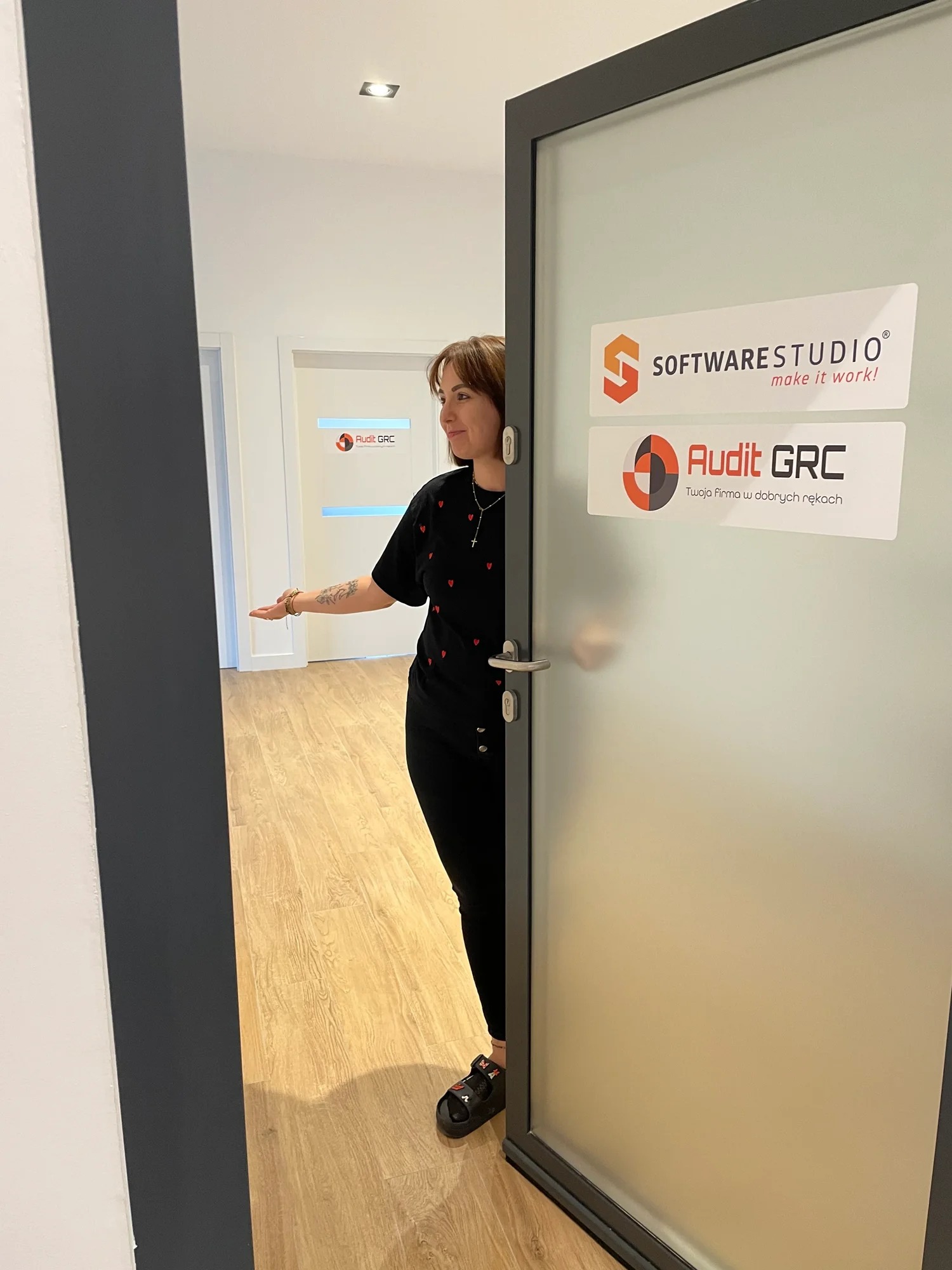 Pracownica biura rachunkowego Audit GRC zaprasza do środka, widoczne logo firmy na szklanych drzwiach wejściowych.