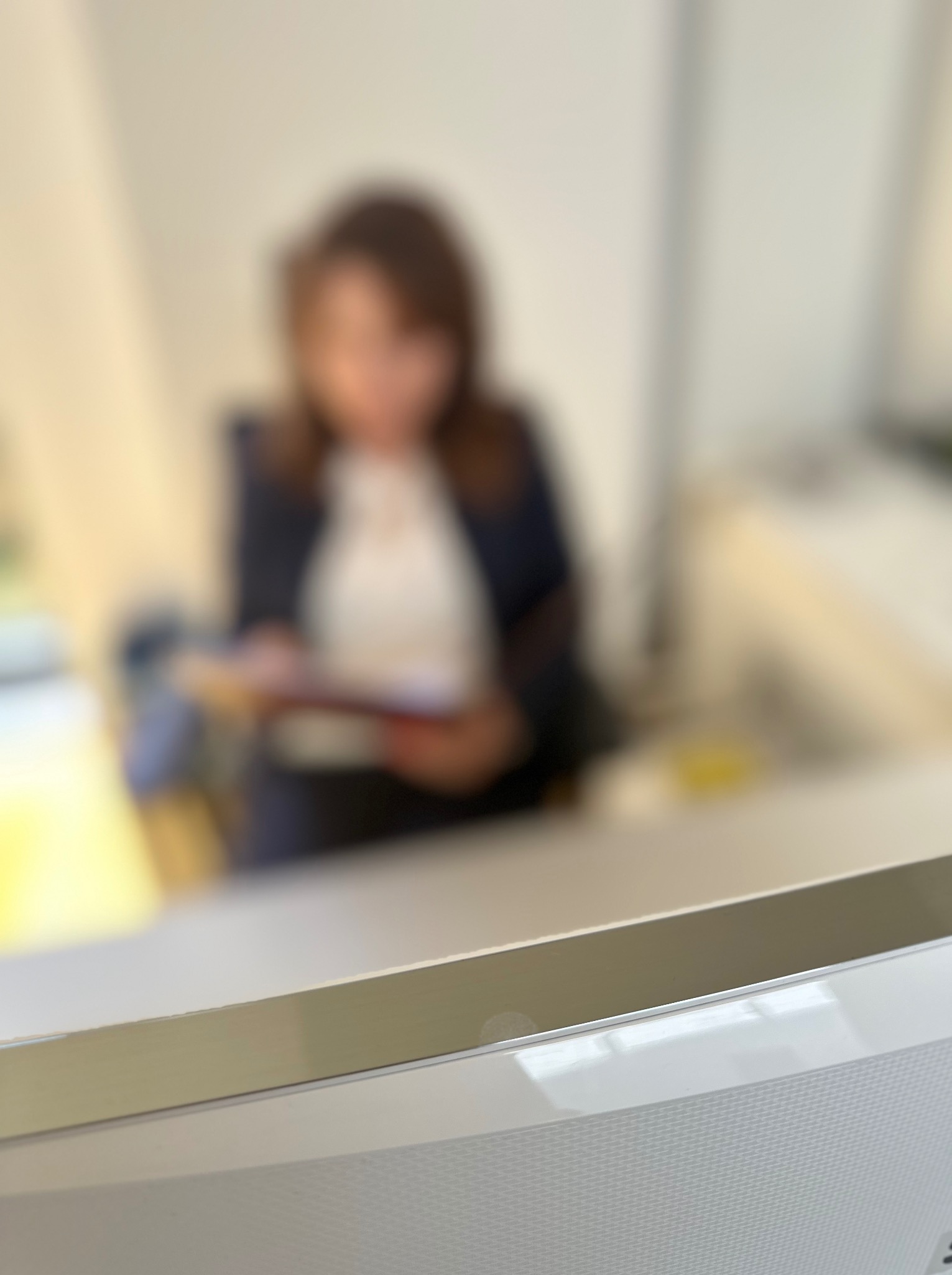 Kobieta w garniturze przegląda dokumenty za biurkiem w jasnym pomieszczeniu, widok zza blatu.