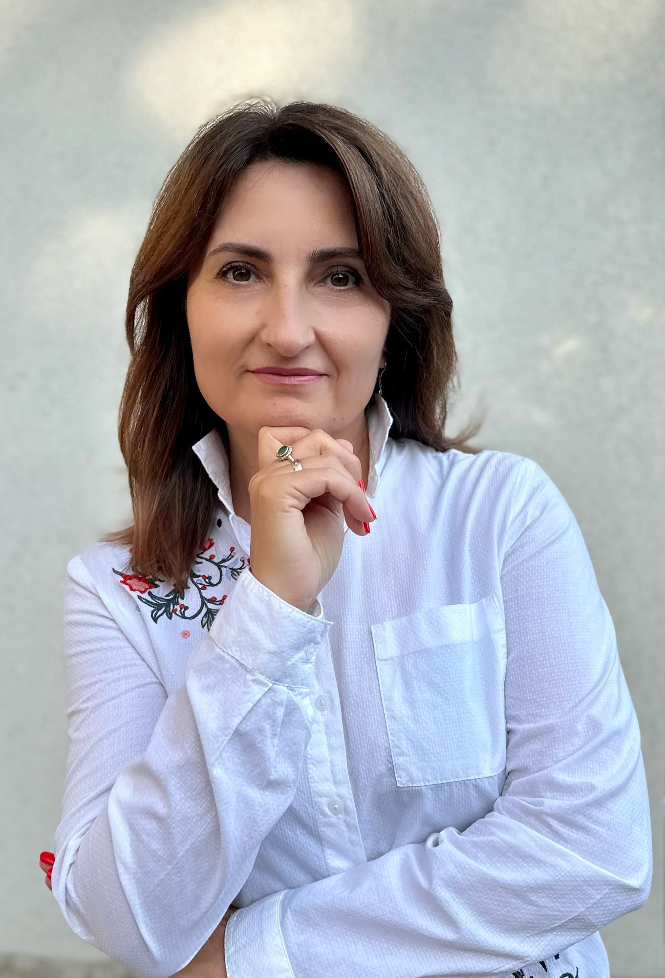 Portret kobiety w białej koszuli z haftem kwiatowym, z pierścionkiem z zielonym kamieniem, opierającej podbródek na dłoni.