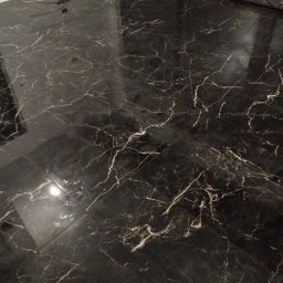 Mateusz Krzemiński - Błyszcząca, czarna podłoga z marmurowym wzorem, świeżo położona w nowym pomieszczeniu z wystającymi kablami elektrycznymi przy ścianie.