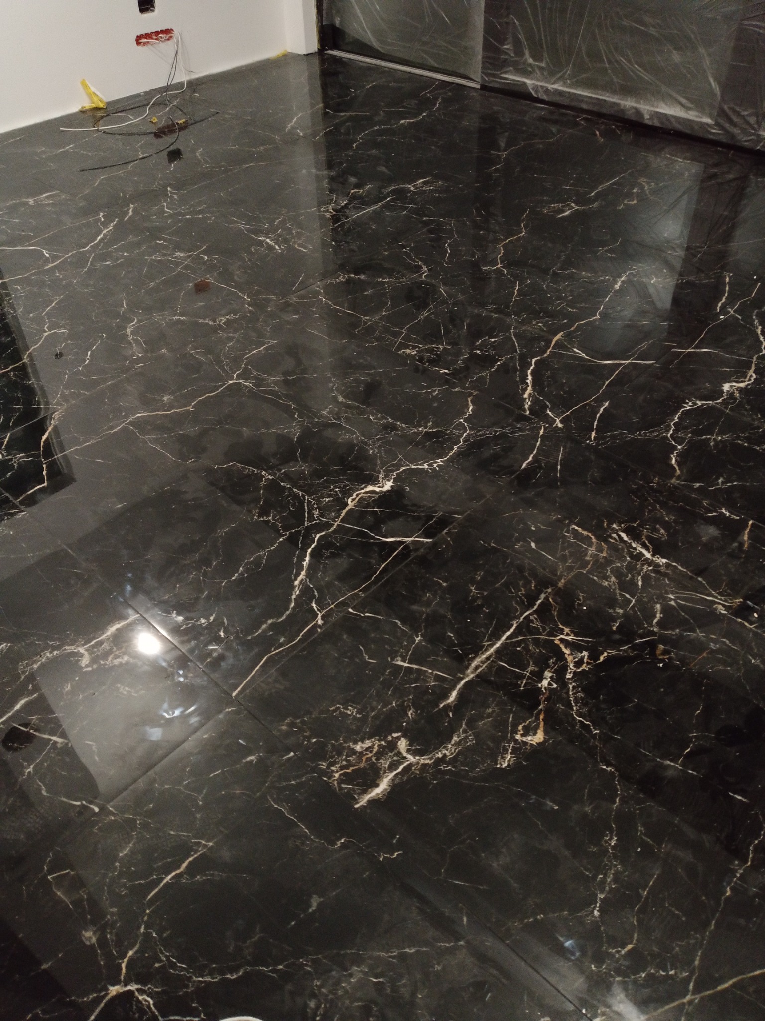 Błyszcząca, czarna podłoga z marmurowym wzorem, świeżo położona w nowym pomieszczeniu z wystającymi kablami elektrycznymi przy ścianie.