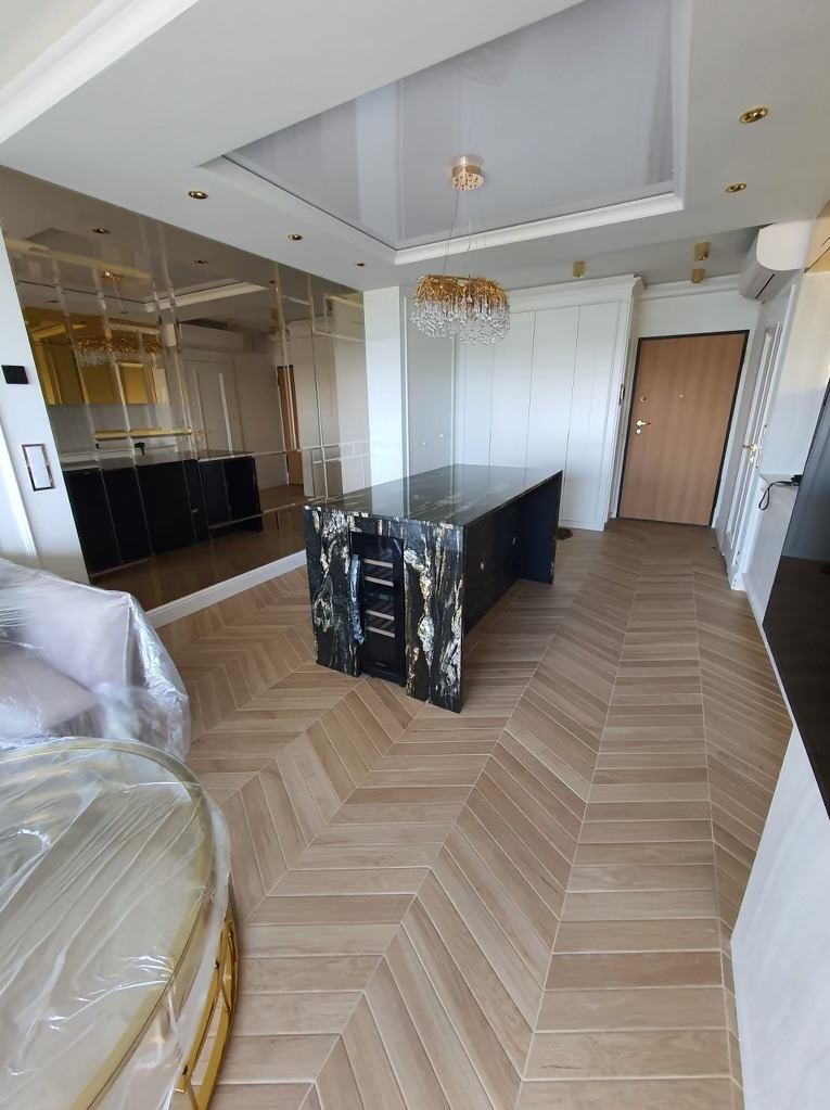 Salon po remoncie z parkietem ułożonym w jodełkę, marmurową wyspą kuchenną z wbudowaną chłodziarką do wina i lustrzaną ścianą