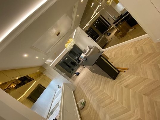 Salon z parkietem ułożonym we wzór jodełki, lustrzane ściany odbijające widok na zewnątrz, nowoczesny żyrandol i meble.