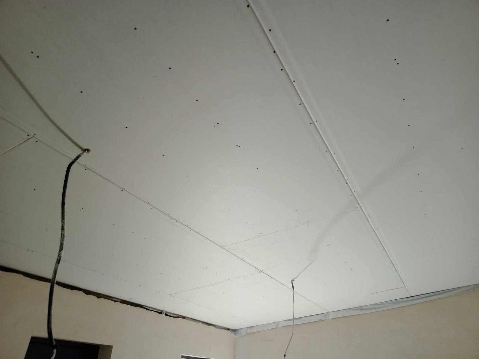 Sufit z płyt kartonowo-gipsowych, widoczne łączenia płyt, wkręty i wystające przewody elektryczne.