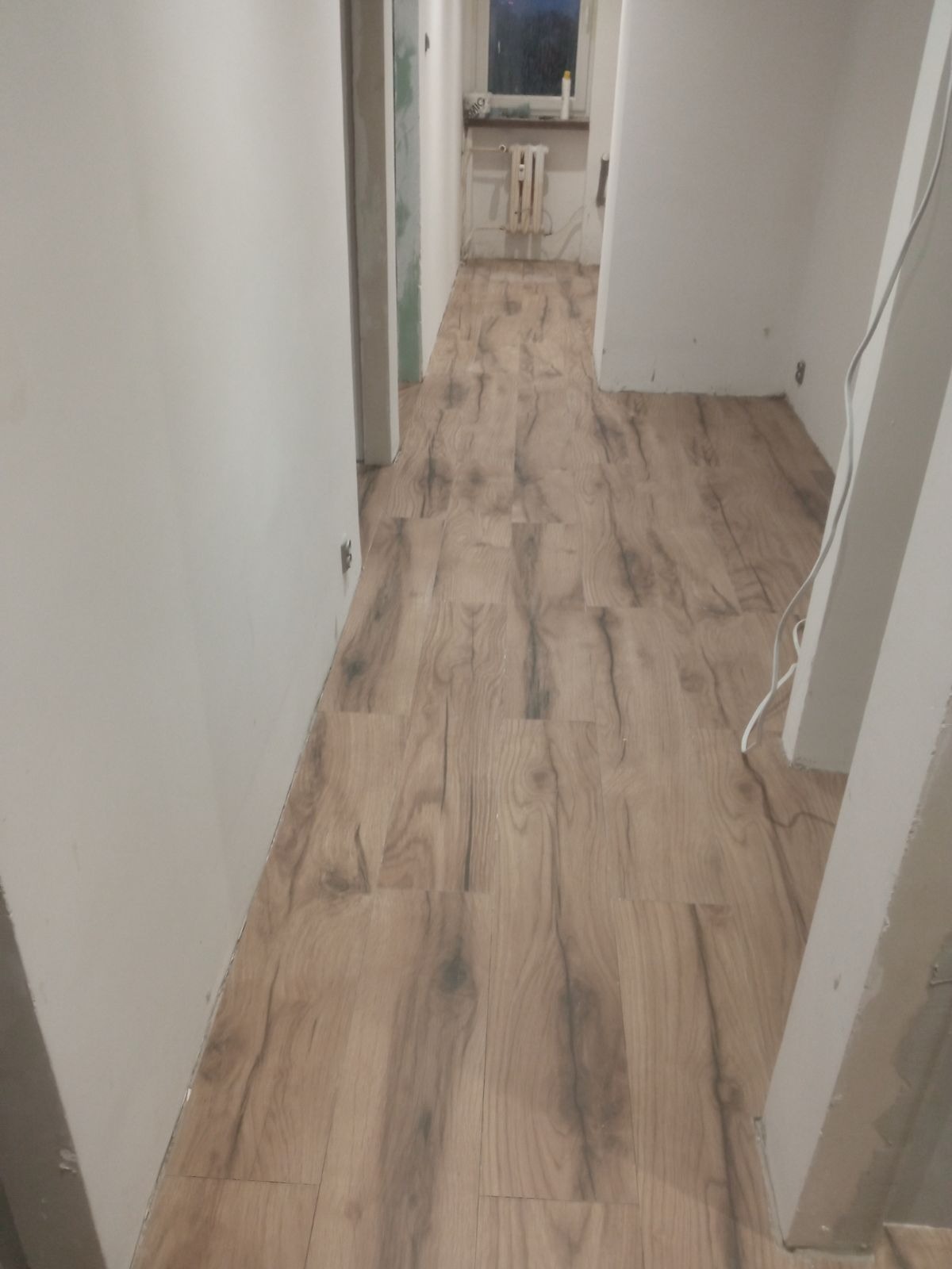 Nowo ułożone panele podłogowe o wzorze drewna w korytarzu mieszkania w Siemianowicach Śląskich, widoczne białe ściany i drzwi w trakcie wykończenia.