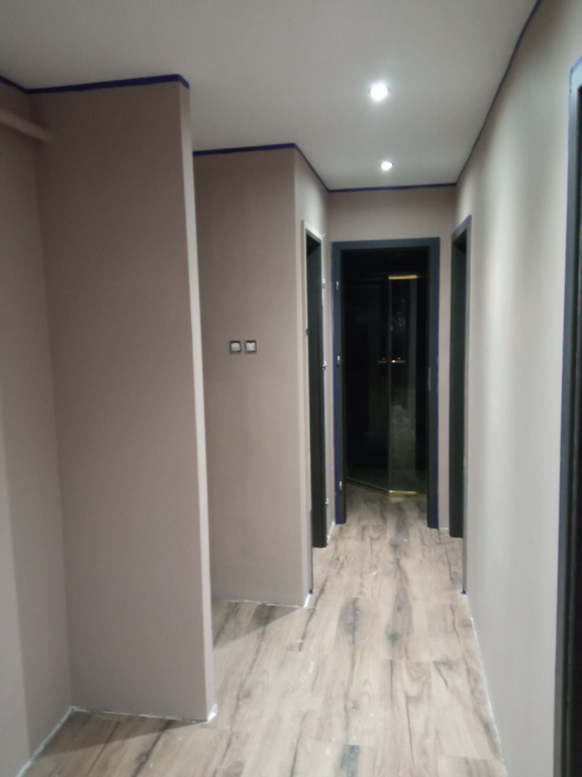 Korytarz po malowaniu ścian na beżowo z niebieskimi akcentami na listwach sufitowych i ościeżnicach, panele podłogowe imitujące drewno.