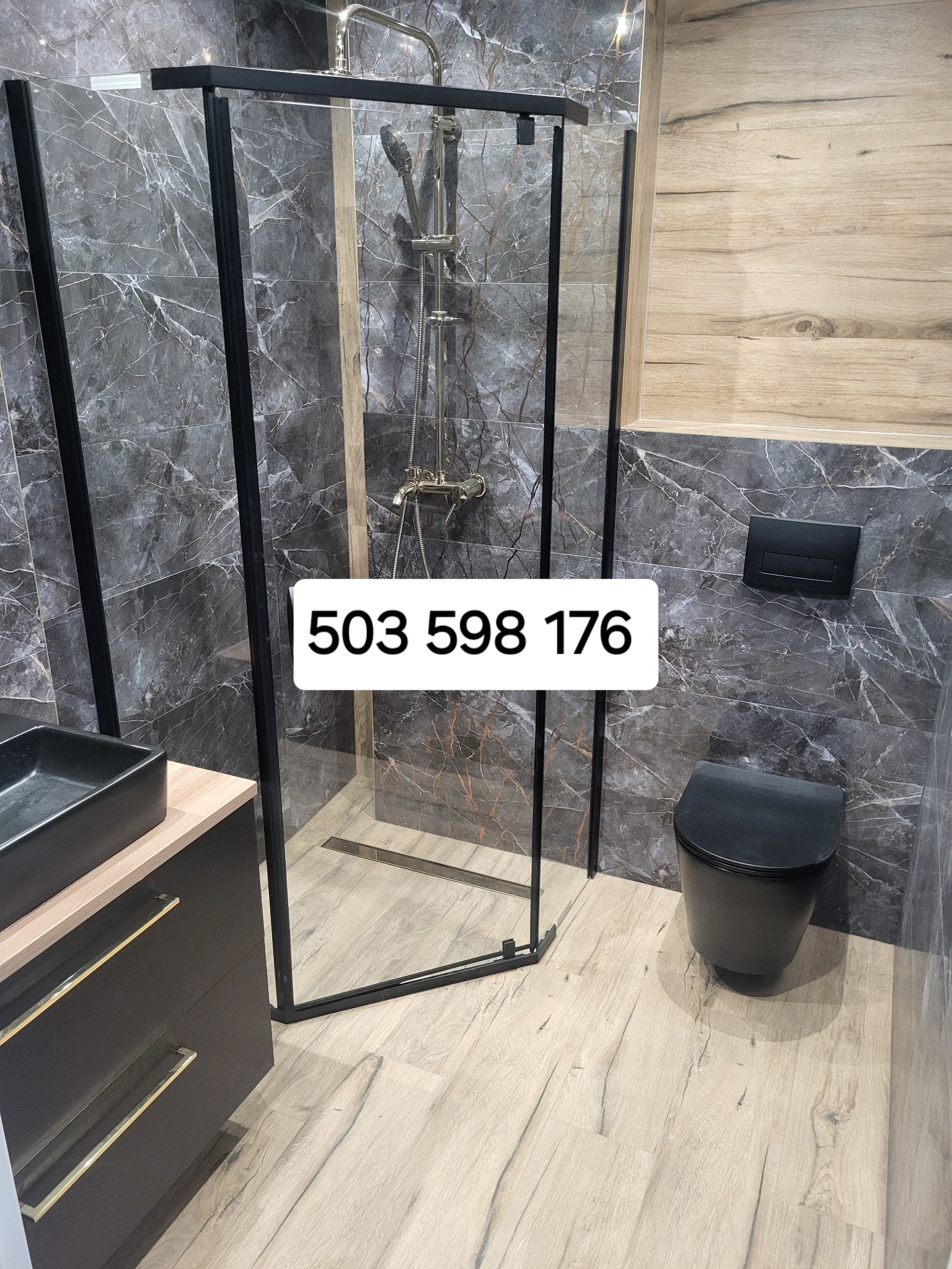 Nowoczesna łazienka z kabiną prysznicową w czarnej ramie, imitacją marmuru na ścianach, drewnopodobnymi płytkami na podłodze i czarną armaturą.