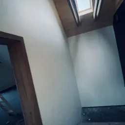 Poddasze w trakcie prac wykończeniowych: widoczne ocieplone skosy, drewniana konstrukcja dachu z oknem dachowym, fragment schodów zabezpieczonych folią i kartonem.