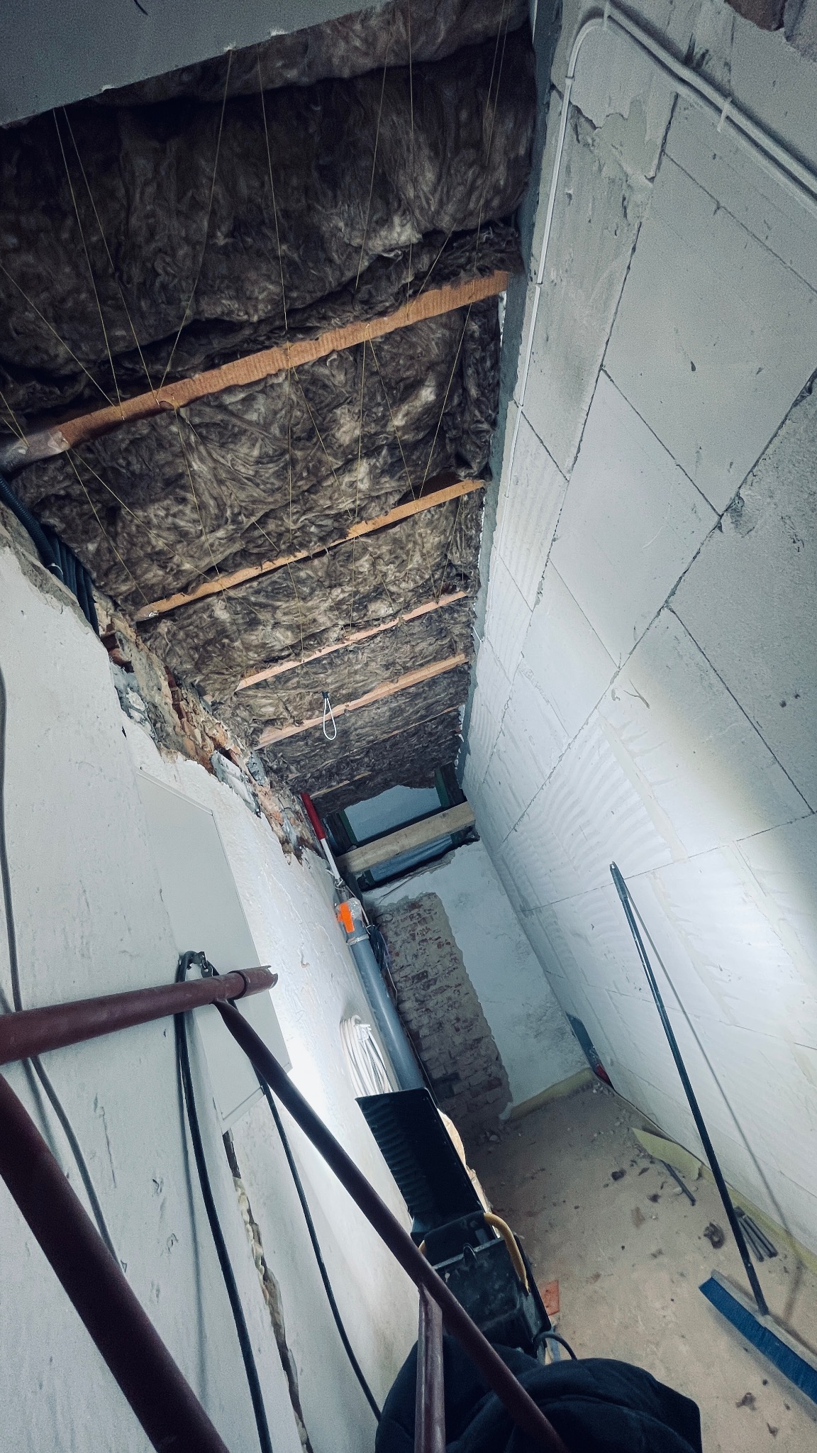 Poddasze w trakcie ocieplania wełną mineralną, widoczne drewniane belki konstrukcyjne, ściany z bloków betonowych i instalacja elektryczna w korytku.