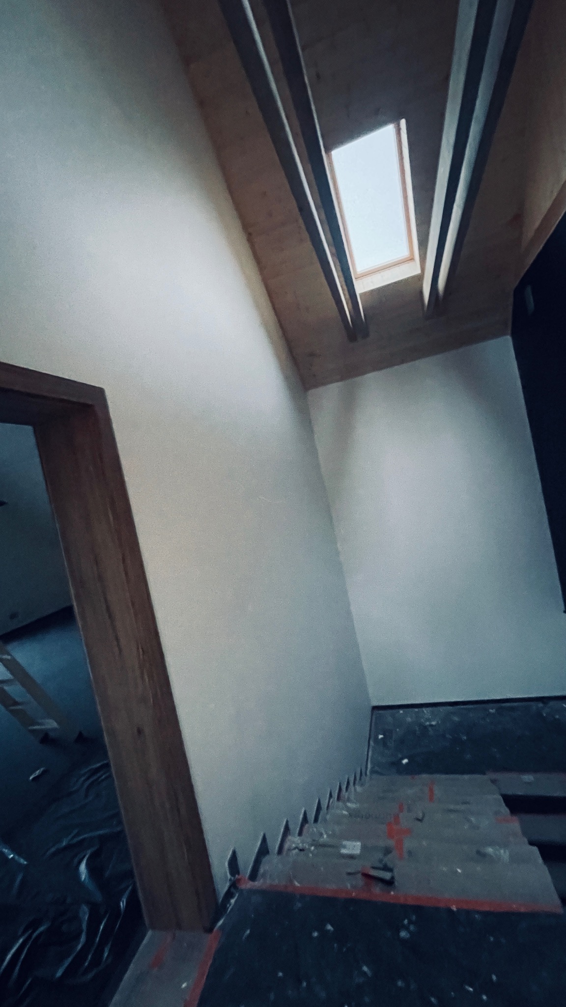 Poddasze w trakcie prac wykończeniowych: widoczne ocieplone skosy, drewniana konstrukcja dachu z oknem dachowym, fragment schodów zabezpieczonych folią i kartonem.