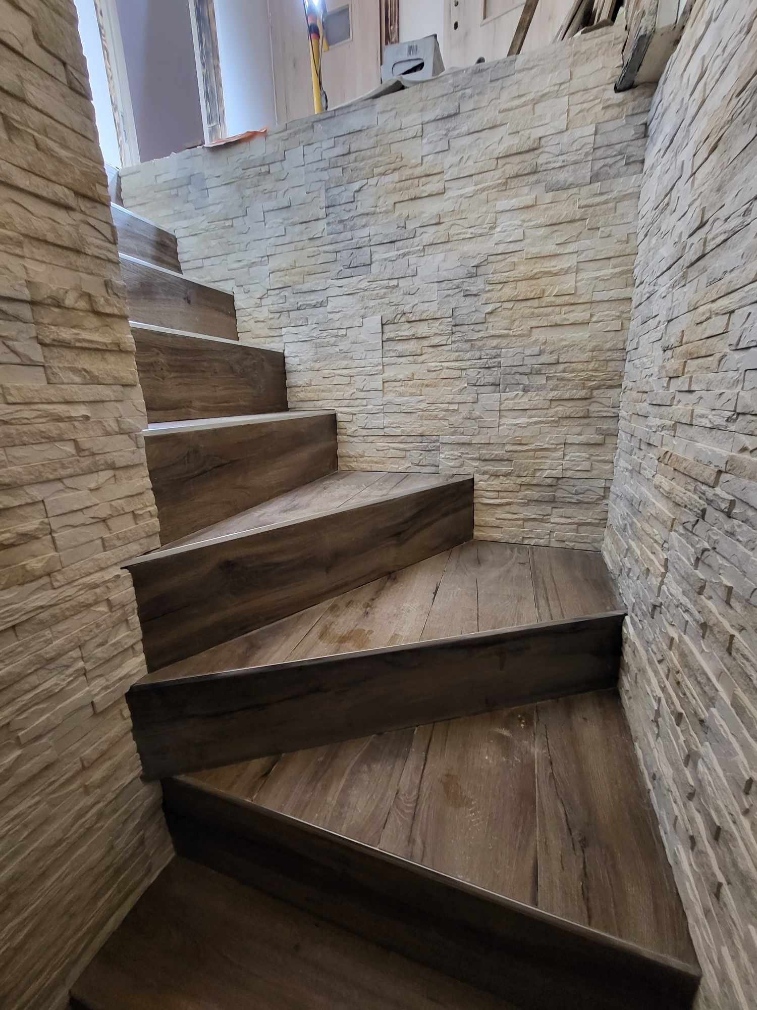 Schody z drewnopodobnymi panelami, wykończone kamienną okładziną ścienną w odcieniach szarości i beżu.