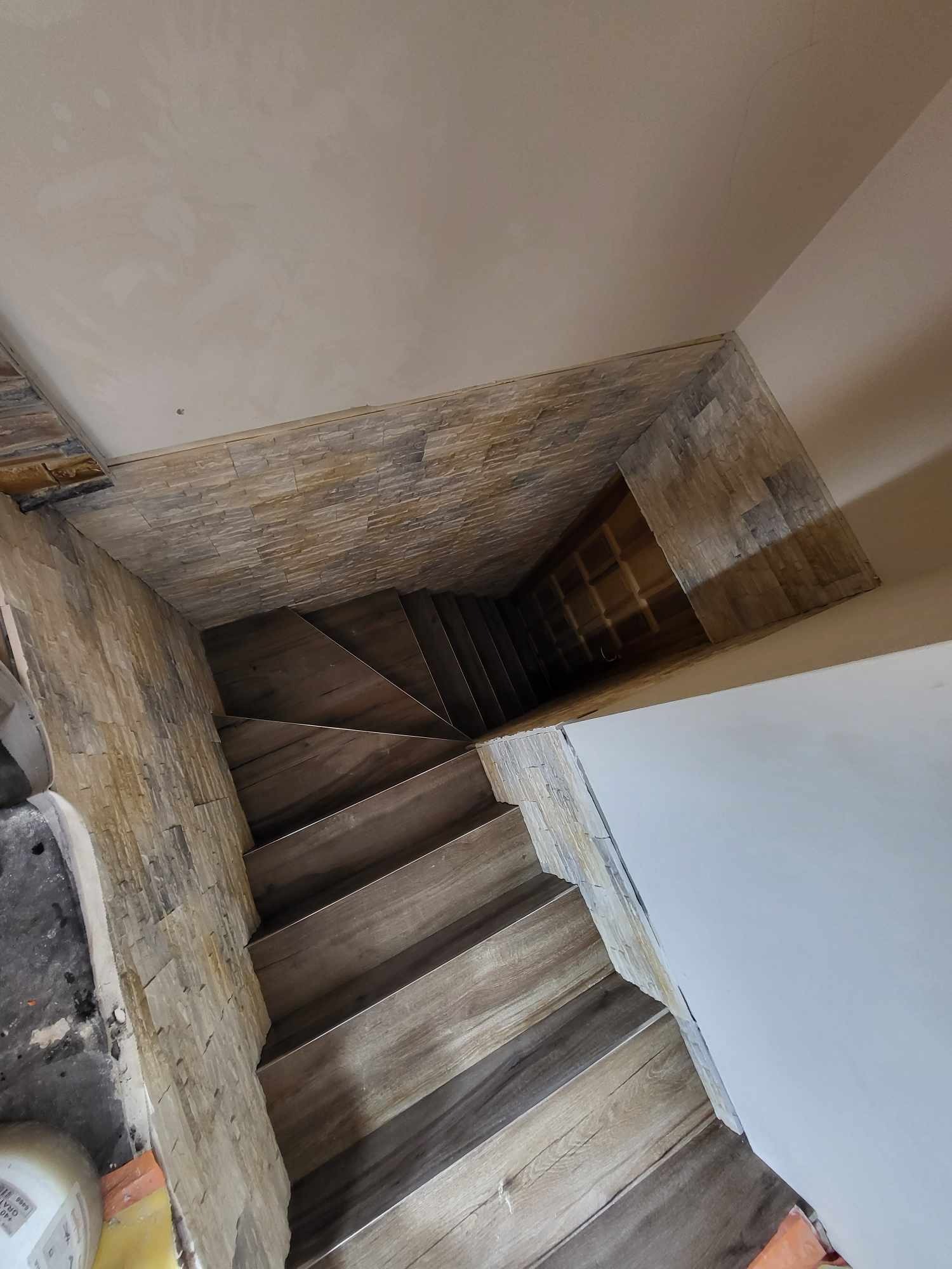 Schody wykończone panelami imitującymi drewno, ściany częściowo pokryte dekoracyjnym kamieniem, widok z góry.