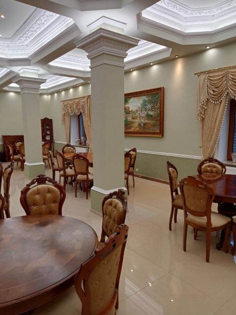 Elegancka jadalnia z klasycznymi meblami, kolumnami dekoracyjnymi i sztukaterią sufitową, oświetlona punktowymi lampami.