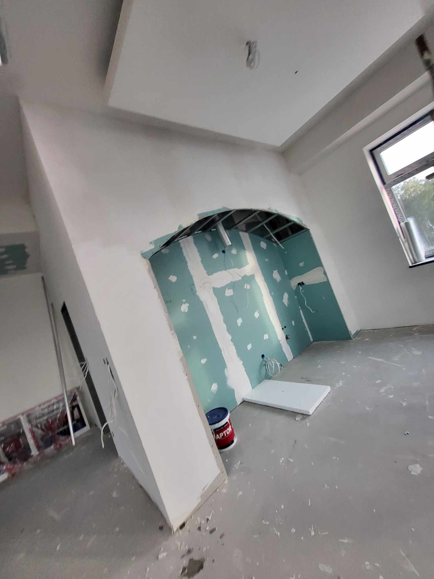 Wnętrze w trakcie remontu: ściany z płyt kartonowo-gipsowych z widocznymi łączeniami szpachlowymi, metalowa konstrukcja łuku, okno dachowe, puszka z masą szpachlową Raptor na podłodze.